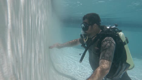 A-professional-pool-cleaner-in-scuba-equipment-cleans-a-pool-while-underwater