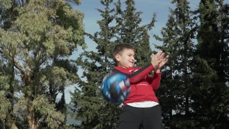 Kaukasischer-Junge-Wirft-Den-Basketball-In-Die-Luft,-Große-Waldbäume-Im-Hintergrund-120fps