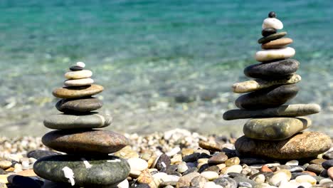 Zen-stacked-rocks-on-a-beach-with-crystal-clear-water-in-the-background-in-Sardinia,-Italy