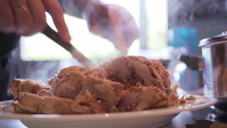Side-view-close-up-of-man's-hands,-cutting-chicken-roll,-steam-comes-in-the-air,-bright-blurry-background
