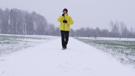 Static-shot-of-male-person-in-winter-clothes-walking-on-a-snowy-rural-path-during-falling-snowflakes