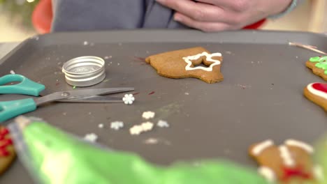 Close-up-on-woman's-hands-drawing-a-star-on-gingerbread-cookie,-using-a-piping-bag-with-white-sugar-icing-4k