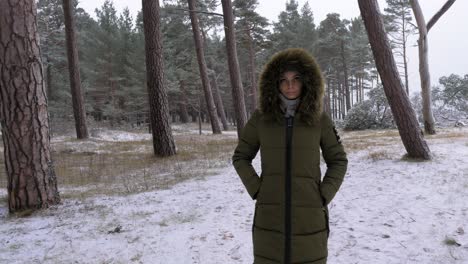 Young-woman-in-green-winter-clothes-walks-in-the-snowy-pine-wood-along-the-sandy-shore-of-the-Baltic-sea-beach,-overcast-day,-medium-handheld-tracking-shot