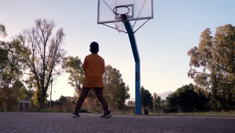Ground-level,-low-view-of-caucasian-boy-trying-basketball-shots,-misses-shot-airball,-on-open-space-basketball-court,-trees-in-the-background
