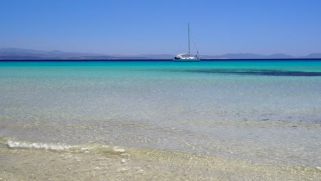 Schöner-Strand-Mit-Einem-Segelboot-Im-Hintergrund-In-Einer-Wunderschönen-Mediterranen-Umgebung-In-Sardinien,-Italien
