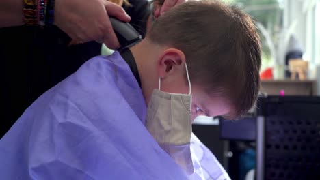 Hair-dresser-cuts-hair-of-caucasian-kid-in-hair-salon,-using-a-trimmer