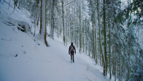 A-lost-man-is-walking-straight-through-a-steep-snowy-forest-with-a-backpack-in-slow-motion