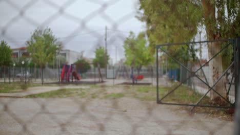 Closed-and-sealed-playground,-view-through-a-wired-fence,-pull-focus-with-shallow-depth-of-field
