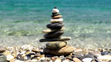 Zen-stacked-rocks-on-a-beach-with-crystal-clear-water-in-the-background-in-Sardinia,-Italy