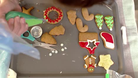 Icing-and-decorating-gingerbread-Christmas-cookies,-using-a-piping-bag-with-coloured-sugar-icing-4K,-high-view