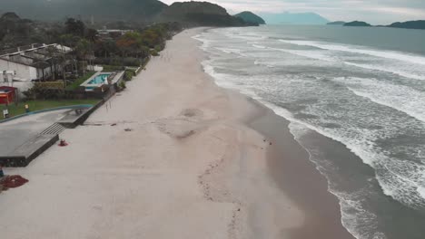 Lateral-drone-footage-of-the-beach,-cloudy-day,-waves,-agitaded-sea,-landscape-of-Juquehy,-Ubatuba,-northern-coast-of-São-Paulo,-Brazil
