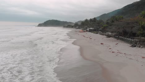 Lateral-drone-footage-of-the-beach,-mountain-in-front-of-the-sea,-cloudy-day,-waves,-landscape-of-Juquehy,-Ubatuba,-northern-coast-of-São-Paulo,-Brazil