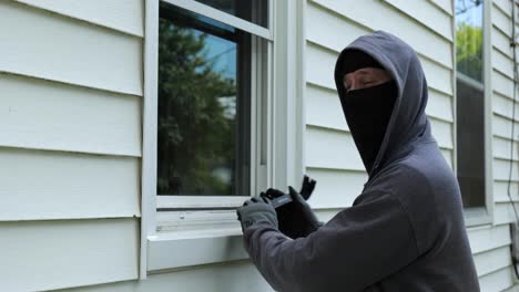 Burglar-pries-open-a-window-with-a-crowbar-and-starts-to-climb-into-a-home