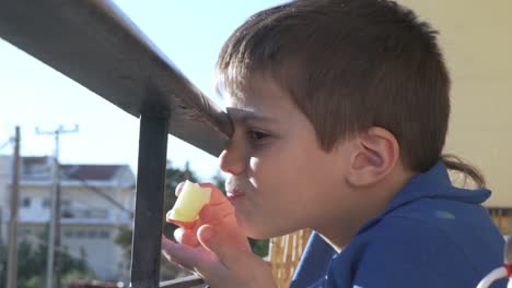 Lindo-Niño-Caucásico,-Comiendo-Manzana-En-El-Balcón-En-Un-Día-Soleado-Y-Brillante