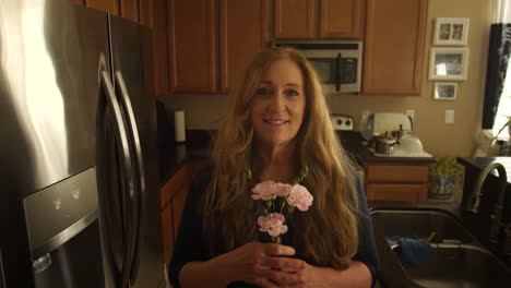 Red-haired-woman-is-handed-a-pink-flower-in-her-kitchen-on-mothers-day