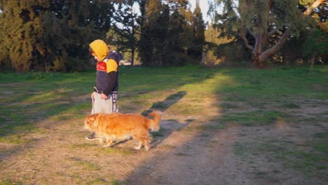 Pan-shot-of-caucasian-boy,-walking-with-his-pet-dog-on-a-leash-,-at-fields-near-Parnitha-forest,-Athens,-Greece
