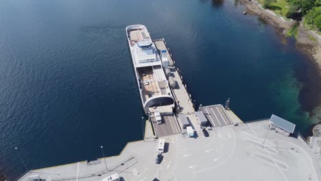 Unloading-ferry-Oppedal-to-road-E-39-at-Lavik-ferry-pier-in-Norway---Beautiful-bacwards-moving-aerial-showing-ferry-before-revealing-harbour-with-ferry-queue-and-road---Norway