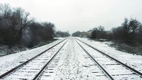 Flurries-blow-towards-the-camera-on-the-ground-level-view-of-the-train-tracks-with-a-slight-pull-up-to-slightly-above