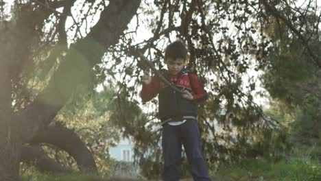 Caucasian-boy-playing-with-wooden-sticks-of-tree's-branch-in-the-forest,-sun-flares-on-screen-120fps