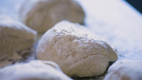 Close-up-of-hand-sprinkling-flour-on-pieces-of-dough-on-table