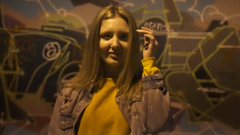 Portrait-of-young-woman-posing-to-camera-at-night-in-front-of-graffiti-wall-slow-motion