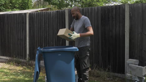 Adult-UK-Asian-Male-Sorting-Cardboard-Beside-Blue-Recycling-Bin-In-Garden