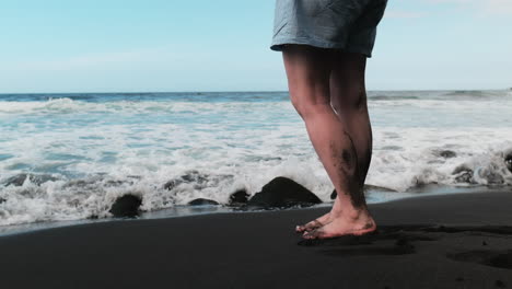 Woman's-legs,-feet-on-black-sand-beach-in-Hawaii,-admiring-ocean