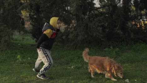 Caucasian-kid-jumping-around-in-the-woods,-playing-with-his-pet-dog,-slow-motion