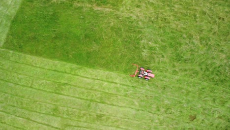 Flying-over-red-lawnmower-tractor-cutting-straight-lines-of-green-grass