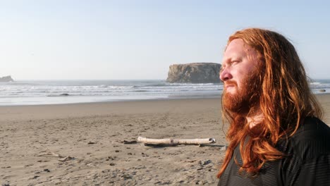 A-red-haired-man-closes-his-eyes-while-looking-out-at-the-beach-enjoying-the-moment