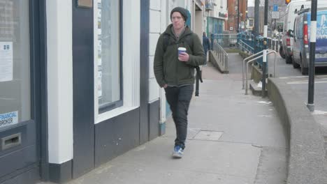 Man-walking-with-coffee-along-street-on-cold-day