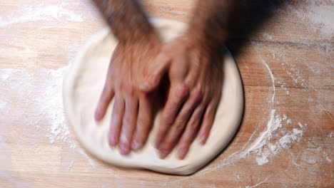 Top-shot-of-Hands-of-a-skilled-chef-roll-out-the-pizza-dough-on-a-wooden-surface-with-flour-around