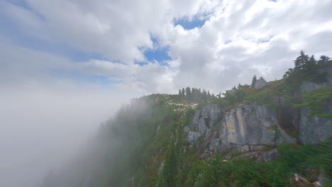 FPV,-Drone-Flying-On-The-Rocky-Cliff-Of-Squamish-Mountain-With-Clouds-And-Fog,-Approaching-Drone-Pilot-On-The-Summit-In-BC,-Canada