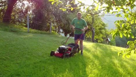 Man-trimming-his-green-lawn-around-his-house-with-red-petrol-rotary-mower