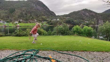 Young-girl-in-pink-playing-with-soap-bubbles-at-lawn---holding-magic-wand-in-her-hand---Outdoor-playtime-by-herself---Static-shot-Norway