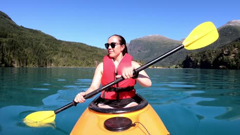 Happy-female-tourist-is-kayaking-lake-Lovatnet-at-a-beautiful-sunny-summer-day---Emerald-green-glacial-lake-with-mountain-background---View-from-kayak-bow-including-slow-paddling-camera-movements