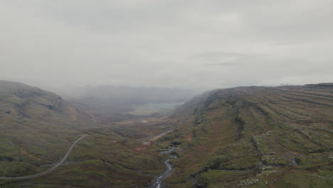 Wide-aerial-of-mountain-steppes,-river-valley,-looking-to-foggy-Iceland-coast