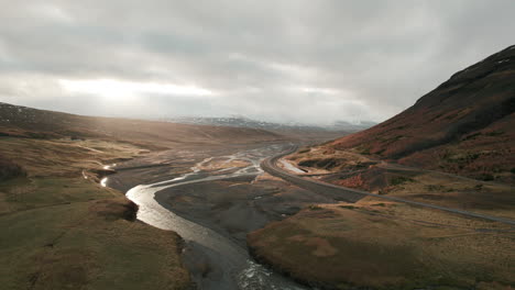 Aerial-parallax-over-gorgeous-Iceland-river-valley,-sunbeams-shining-through-clouds