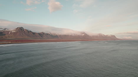 Aerial-view-over-ocean-looking-towards-dramatic-mountains-on-Iceland-shoreline