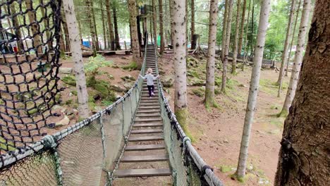 Cute-young-blonde-girl-waking-on-rope-suspension-bridge-inside-woods-of-Mikkelparken-theme-park---Norway