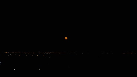 Night-footage-of-orange-full-moon-over-cityscape,-near-international-airport-of-Athens-4k