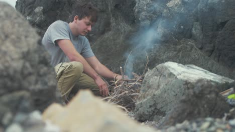 Young-man-lighting-campfire-alone-on-rocky-seaside-shoreline