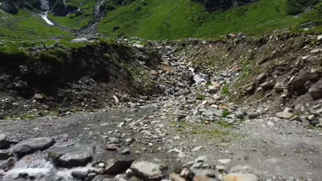 Volando-Bajo-Hacia-Atrás-Sobre-Un-Arroyo-De-Agua-En-Austria-Con-Muchas-Rocas