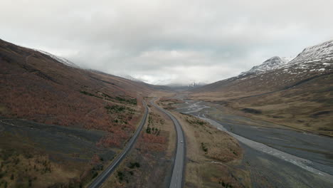 Aerial-rise-looking-down-on-cars-driving-valley-highway-through-Iceland-mountain-range