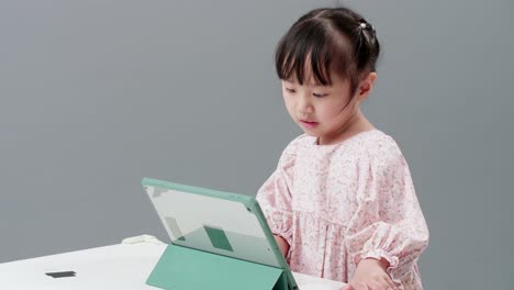 Little-Asian-girl-study-online-e-learning-system-using-tablet-for-video-call,-paying-attention-to-online-lesson,-teacher-and-classmates