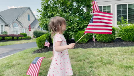 Una-Niña-Ondea-Banderas-Americanas-En-Su-Patio-Delantero-Antes-De-Un-Desfile-O-Celebración
