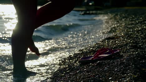 Person-walking-on-the-beach-at-sunset-during-summer-vacation-holidays-slow-motion,-closeup-of-legs-and-feet-with-slippers-in-the-sea-water,-4k-video