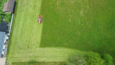 Red-lawnmower-moving-green-meadows-beside-urbane-settlement