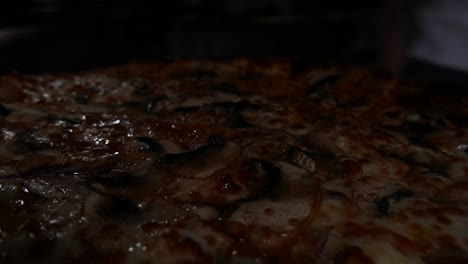pov-of-Pizza-dough-with-onion-mushrooms-and-mozzarella-cheese-comes-out-of-the-oven-on-a-metal-tray-towards-a-wooden-surface-surrounded-by-fresh-vegetables