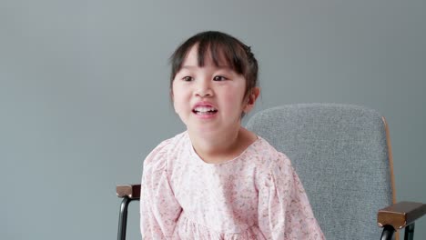 Fröhliche-Und-Fröhliche-Asiatische-Kinder-Im-Alter-Von-3-Jahren-Sitzen-Auf-Einem-Stuhl-Vor-Dem-Grauen-Hintergrund